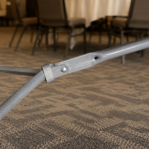 Close-up of the gravity lock mechanism on a commercial folding table in a hospitality meeting room.